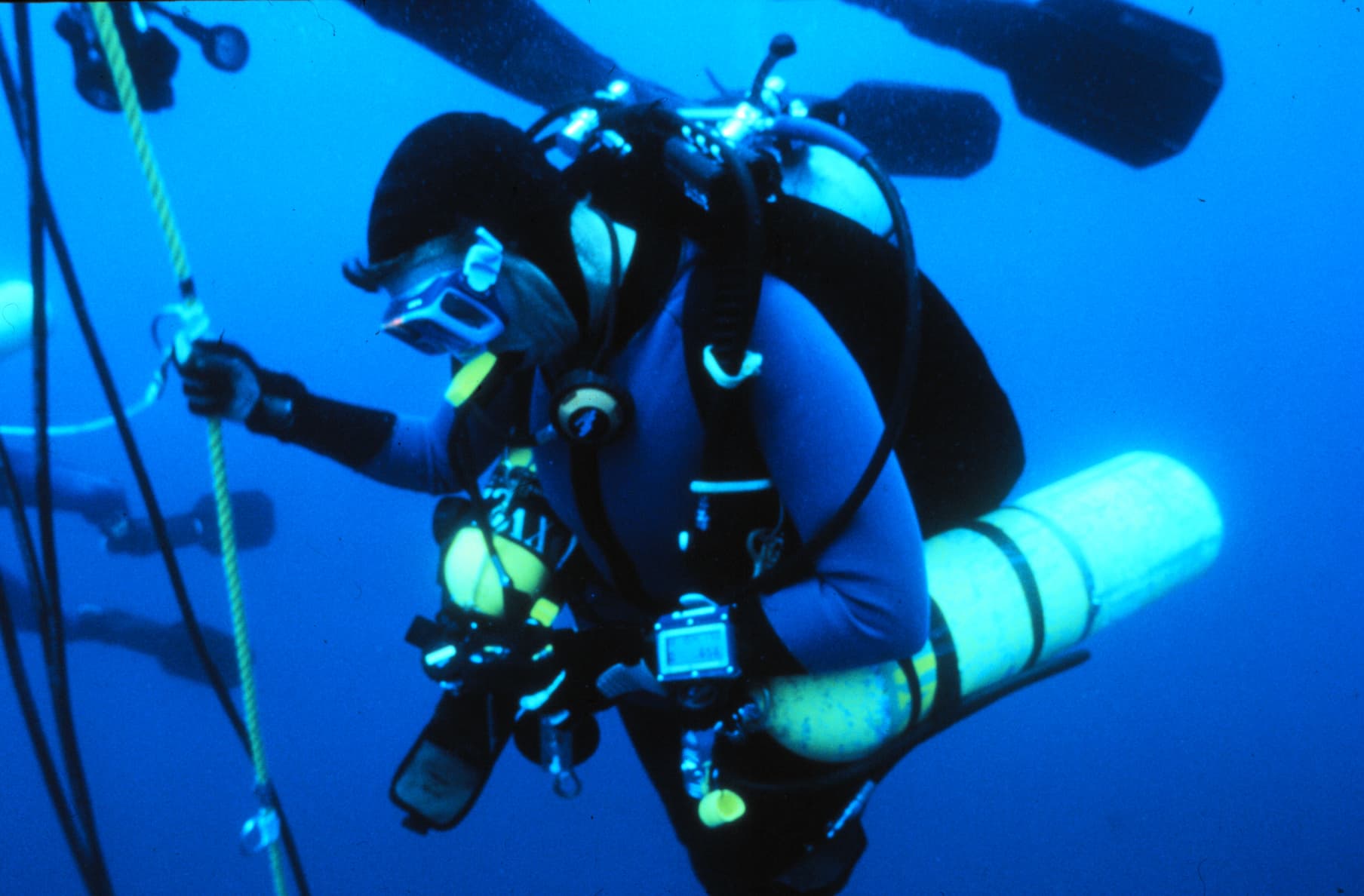 A technical diver on twin cylinders and a stage bottle holds the line during a decompression stop